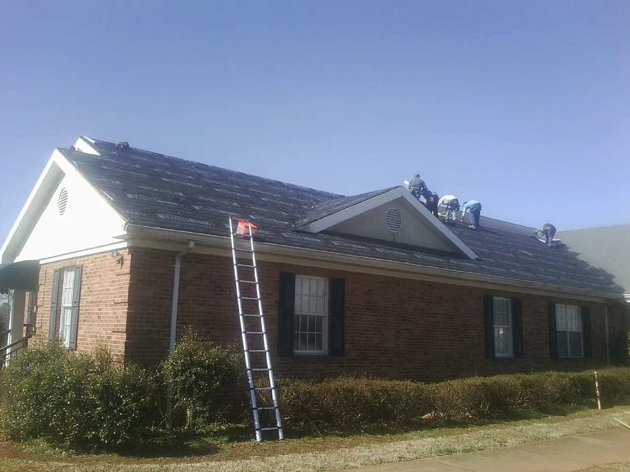 Crew tearing shingles off a brick ranch roof with a ladder set — Emergency Roof Repair work by our crew in Ponderay