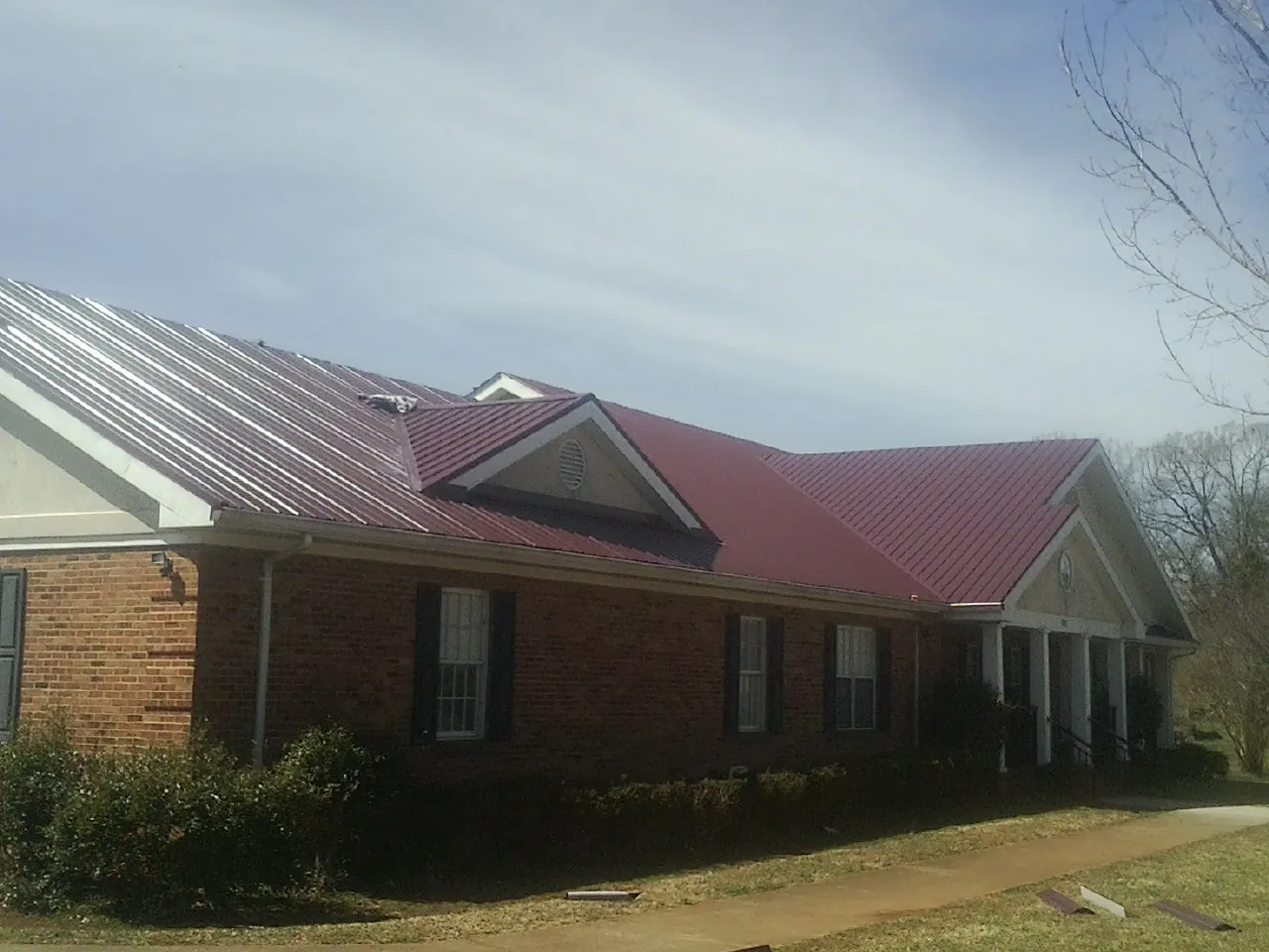 Red metal roof with gabled entries on a long brick building, from a Hail Damage Roof Repair job in Ponderay