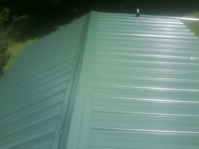New green metal panels meeting at the ridge of a roof — Flat Roof Repair work by our crew in Ponderay