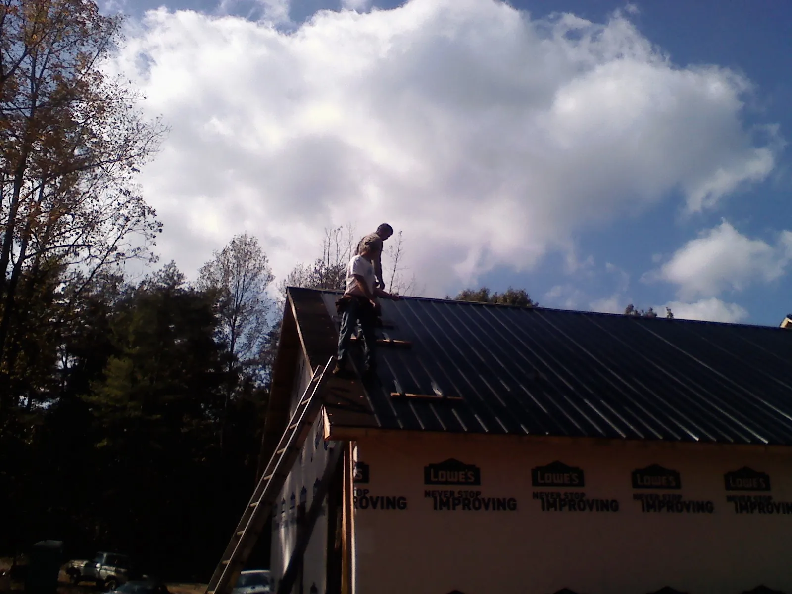 Roofer fastening dark metal panels high against a cloudy sky, from a Roof Inspection job in Ponderay