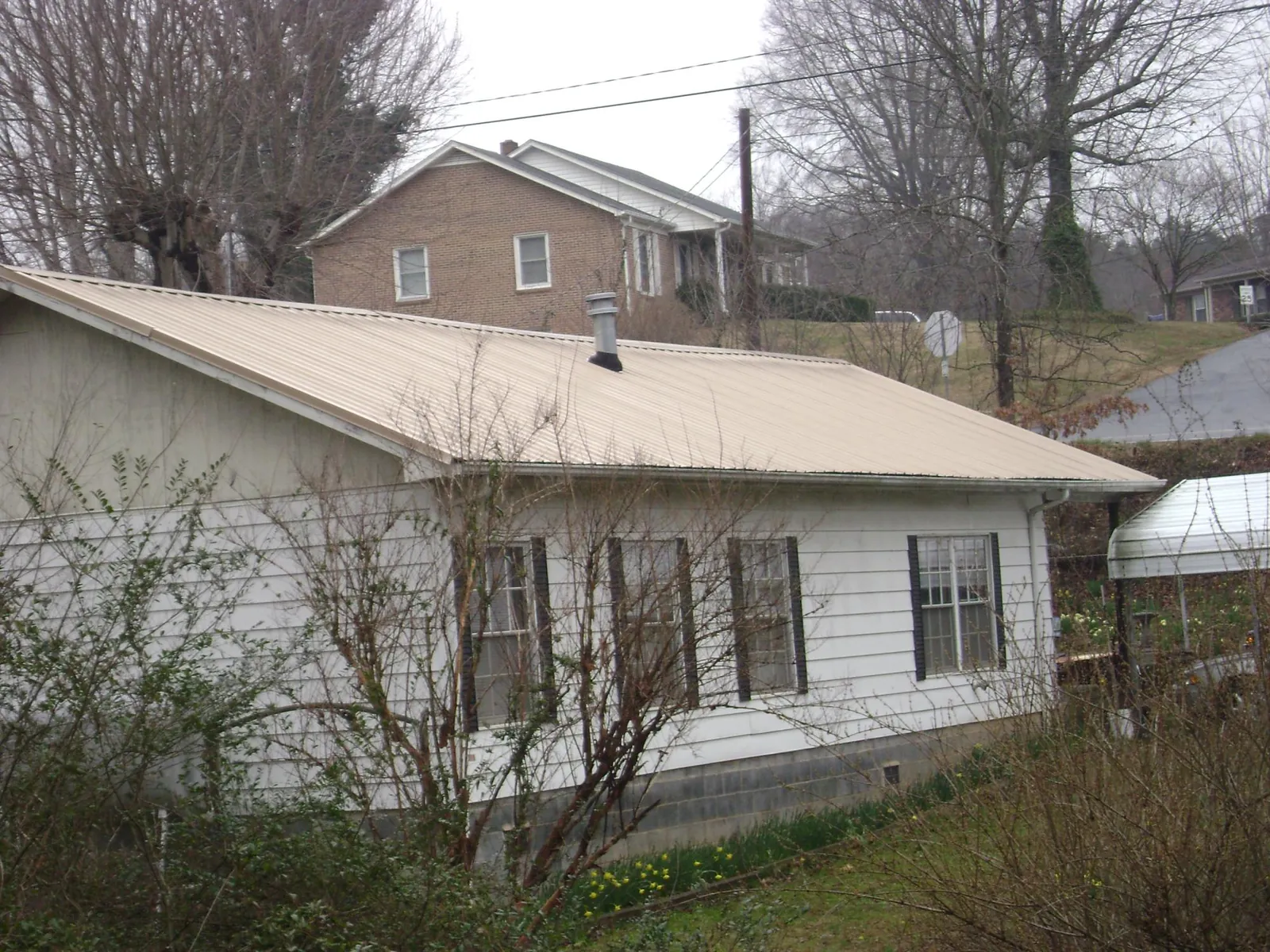 Tan metal roof on a white sided house set into a hillside — Commercial Roofing by Roofing Brothers in Ponderay